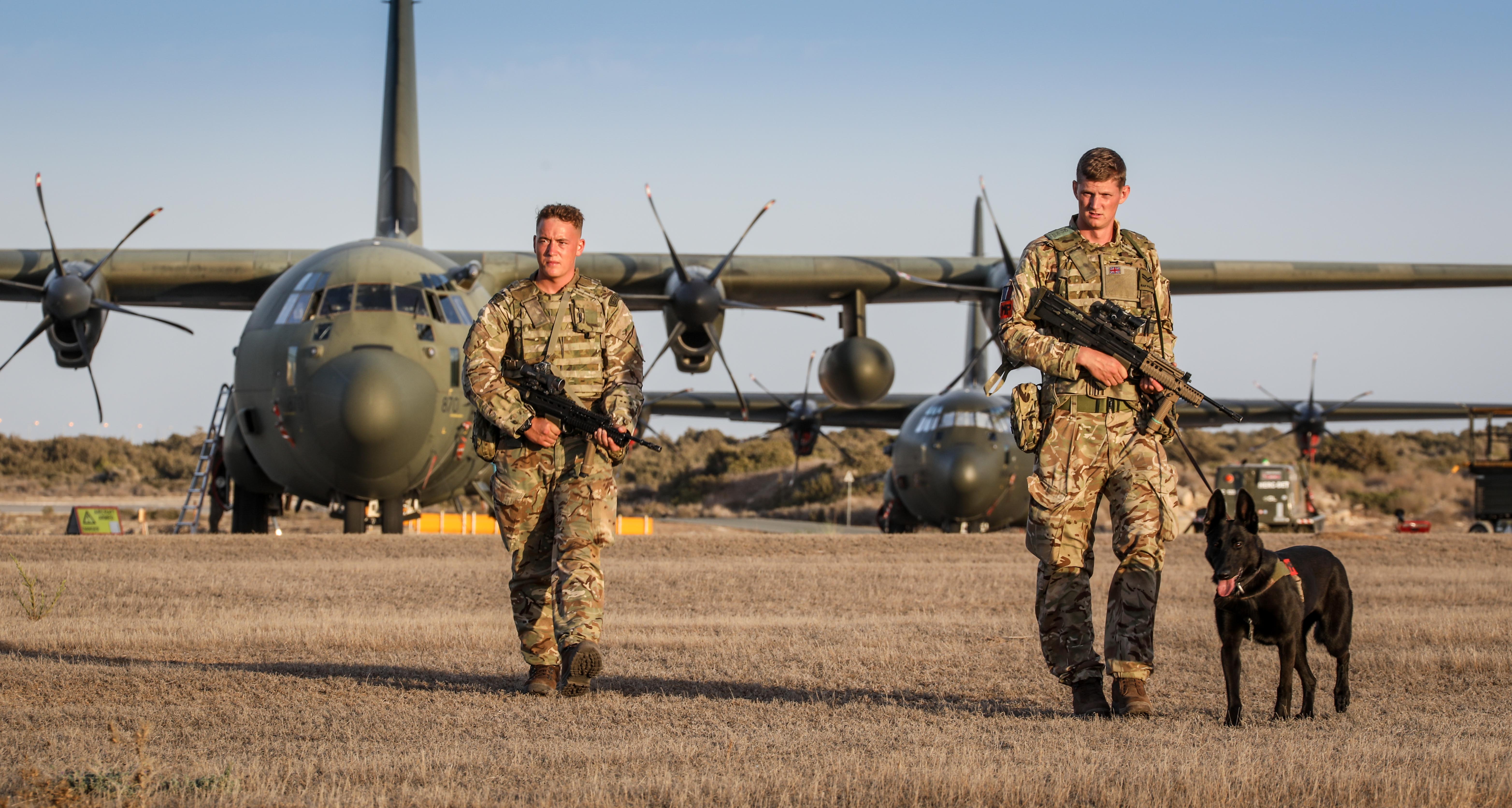 Personnel walk with Military Working Dogs and rifles, in front of Atlas aircraft.